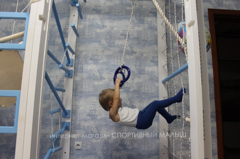Активный малыш занимается гимнастикой дома на специально оборудованном в городской квартире спортивном уголке